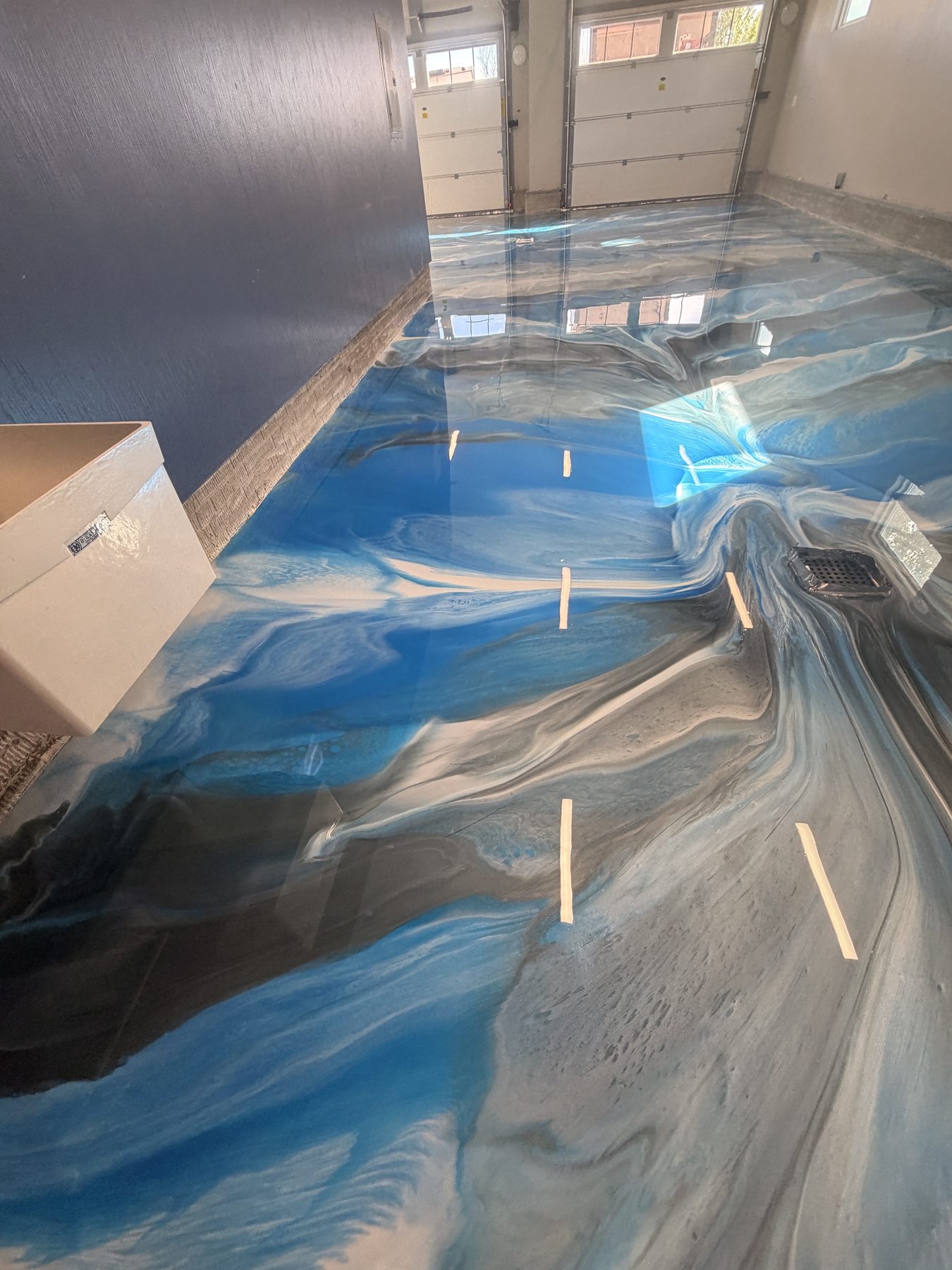 Swirled blue, white and charcoal metallic epoxy floor running to two garage doors